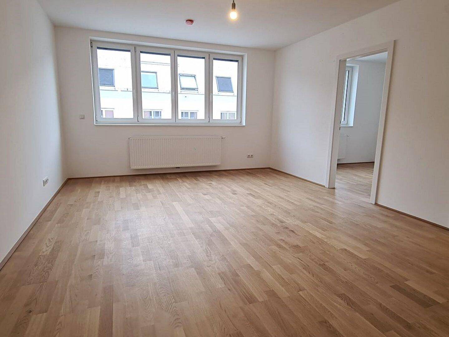 Geräumiges Wohnzimmer mit hellem Parkettboden und großen Fenstern, bereit zur Einrichtung.