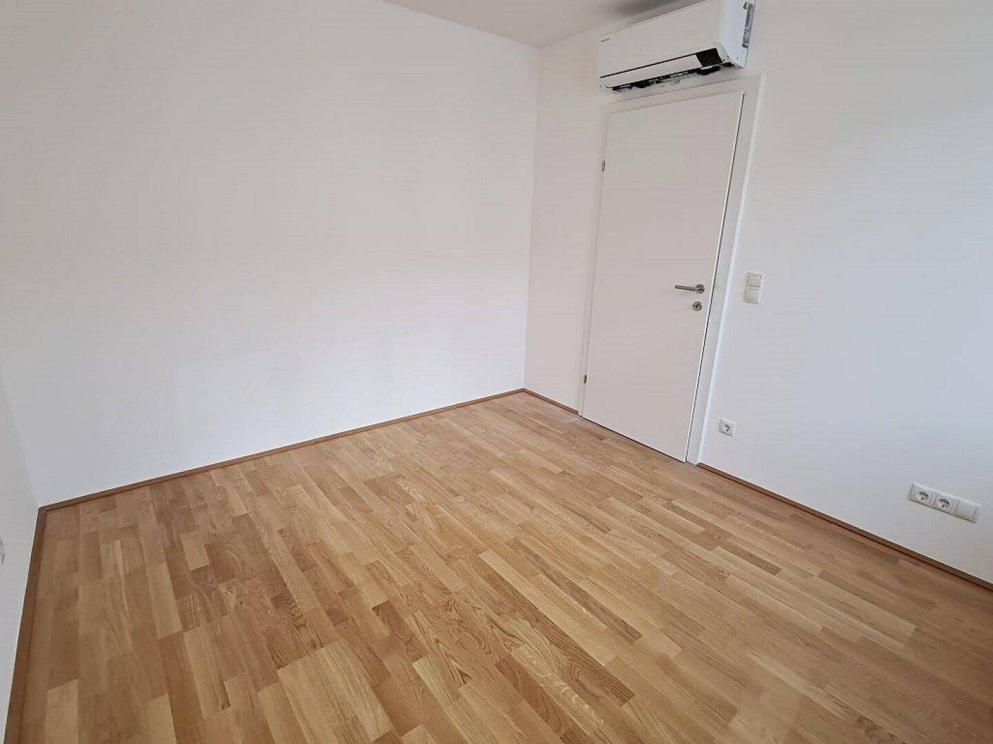 Geräumiges Schlafzimmer mit Parkettboden, Klimaanlage und weiß gestrichenen Wänden.