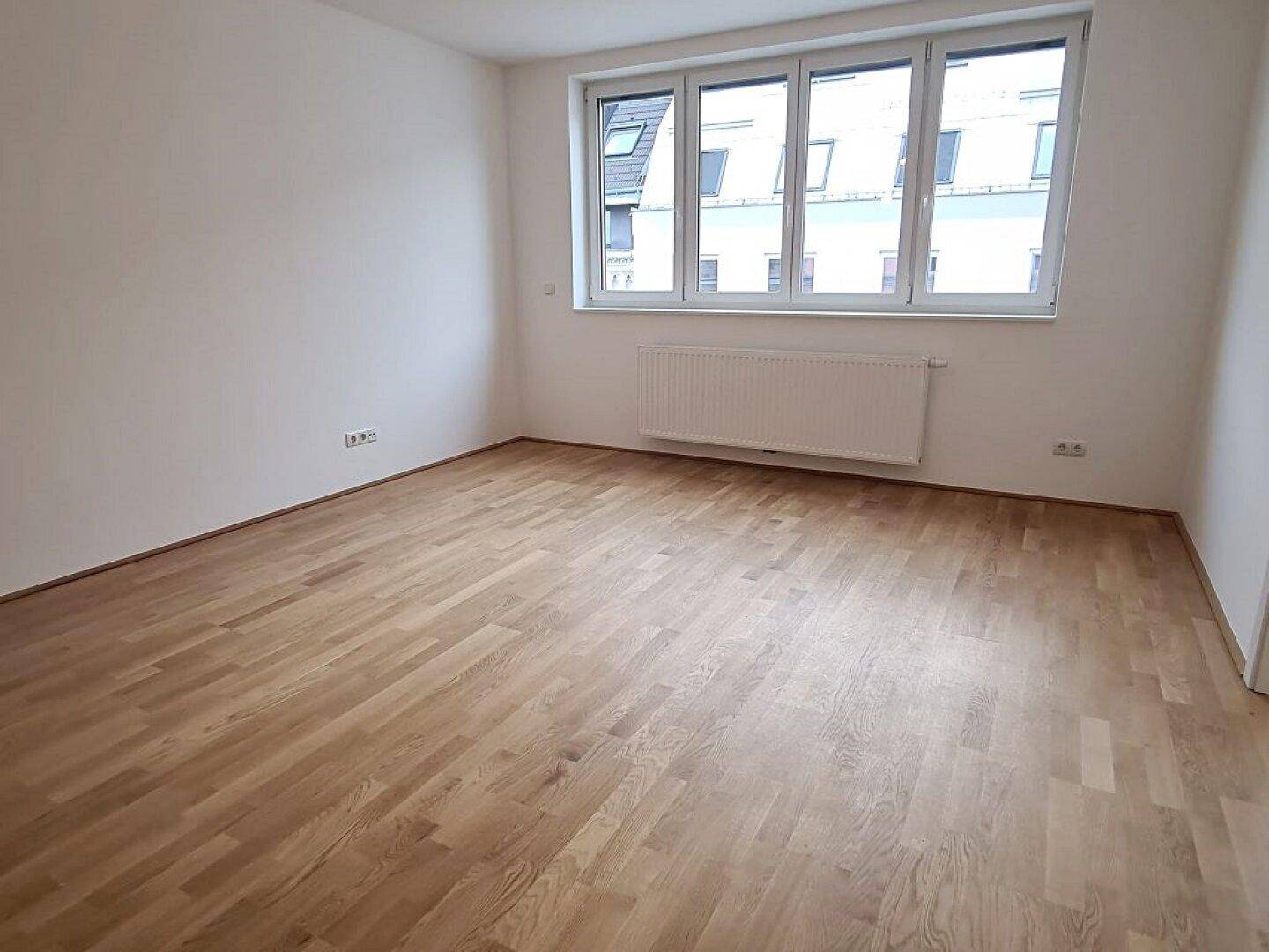 Geräumiges Zimmer mit hellem Parkettboden und großen Fenstern, ideal für ein Wohn- oder Schlafzimmer.