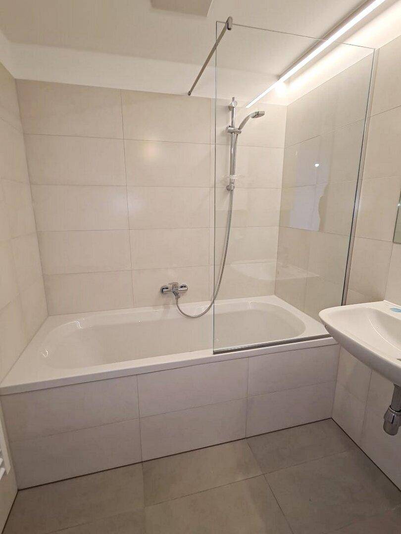 Badewanne mit Glasduschwand in einem modern gefliesten Badezimmer, sauber und funktional.