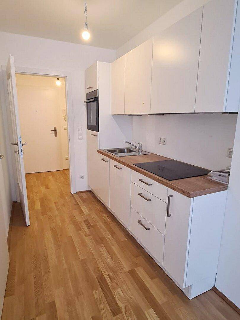 Moderne Kochnische mit weißen Schränken, Holz-Arbeitsplatte und Induktionskochfeld, praktisch und kompakt.