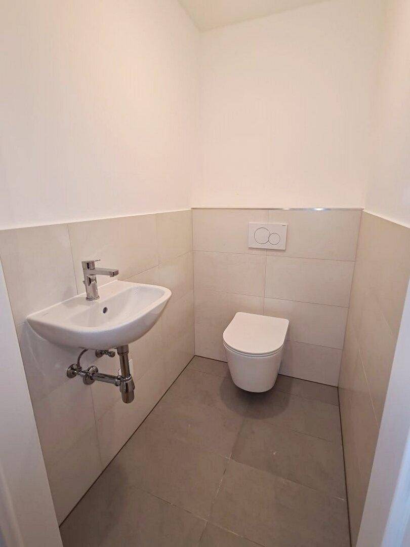 Separates Gäste-WC mit modernen Fliesen, wandhängendem WC und kleinem Handwaschbecken.