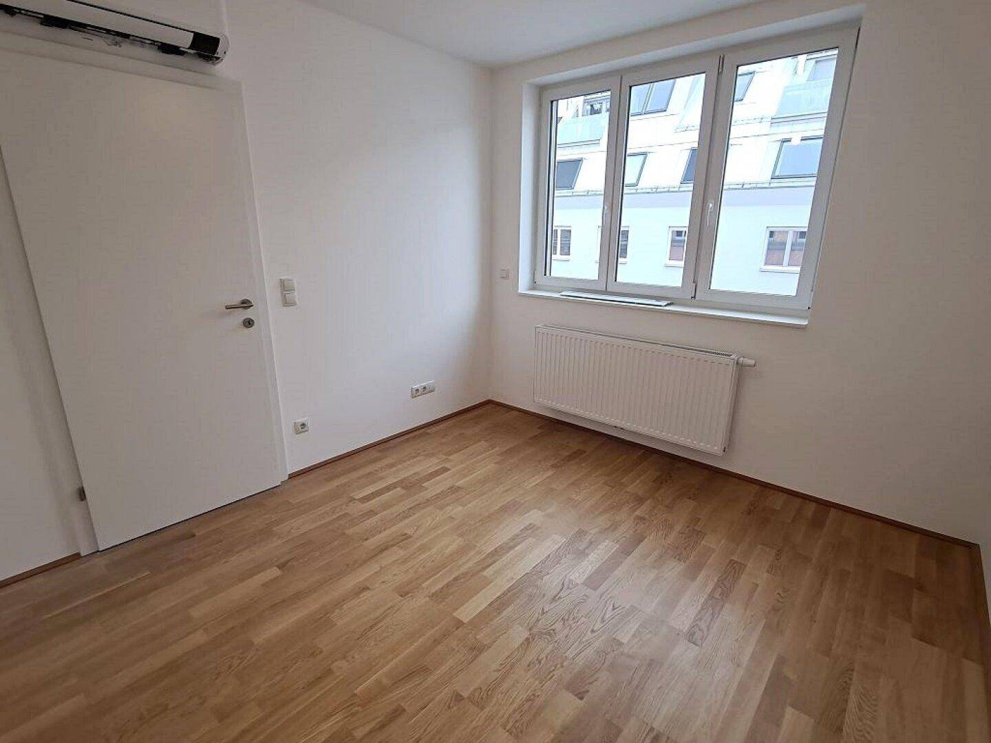 Helles Schlafzimmer mit Parkettboden, Klimaanlage und großem Fenster, ideal für Komfort.
