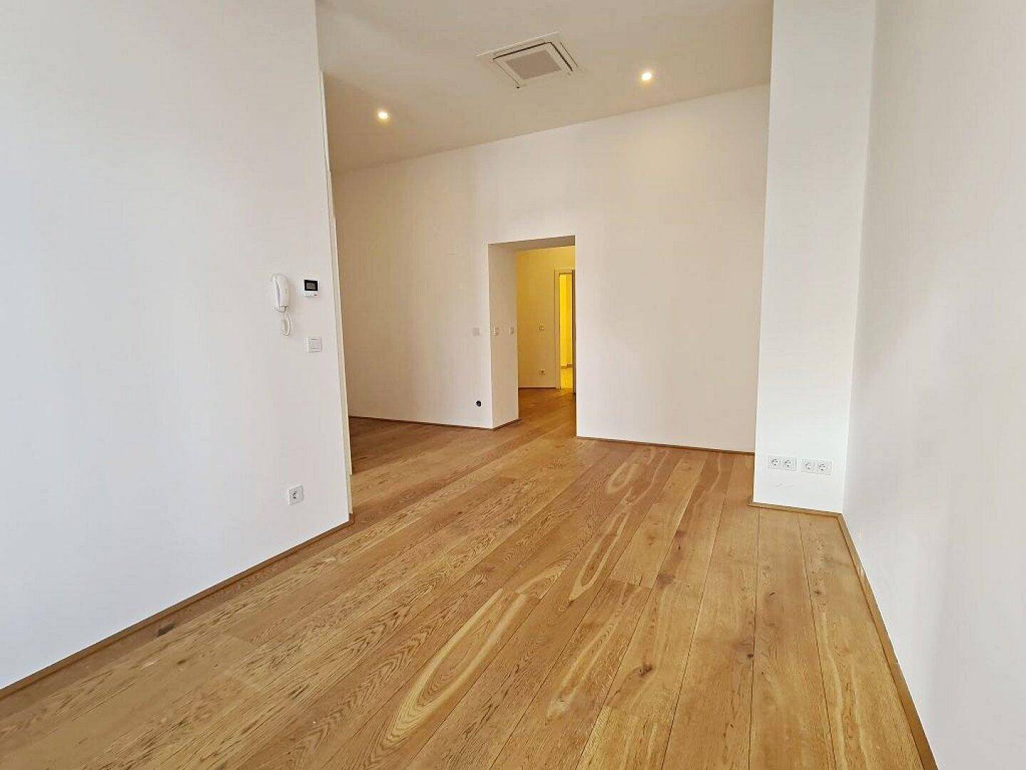 Geräumiger Raum mit Holzboden, weißen Wänden und einer Gegensprechanlage an der Wand.