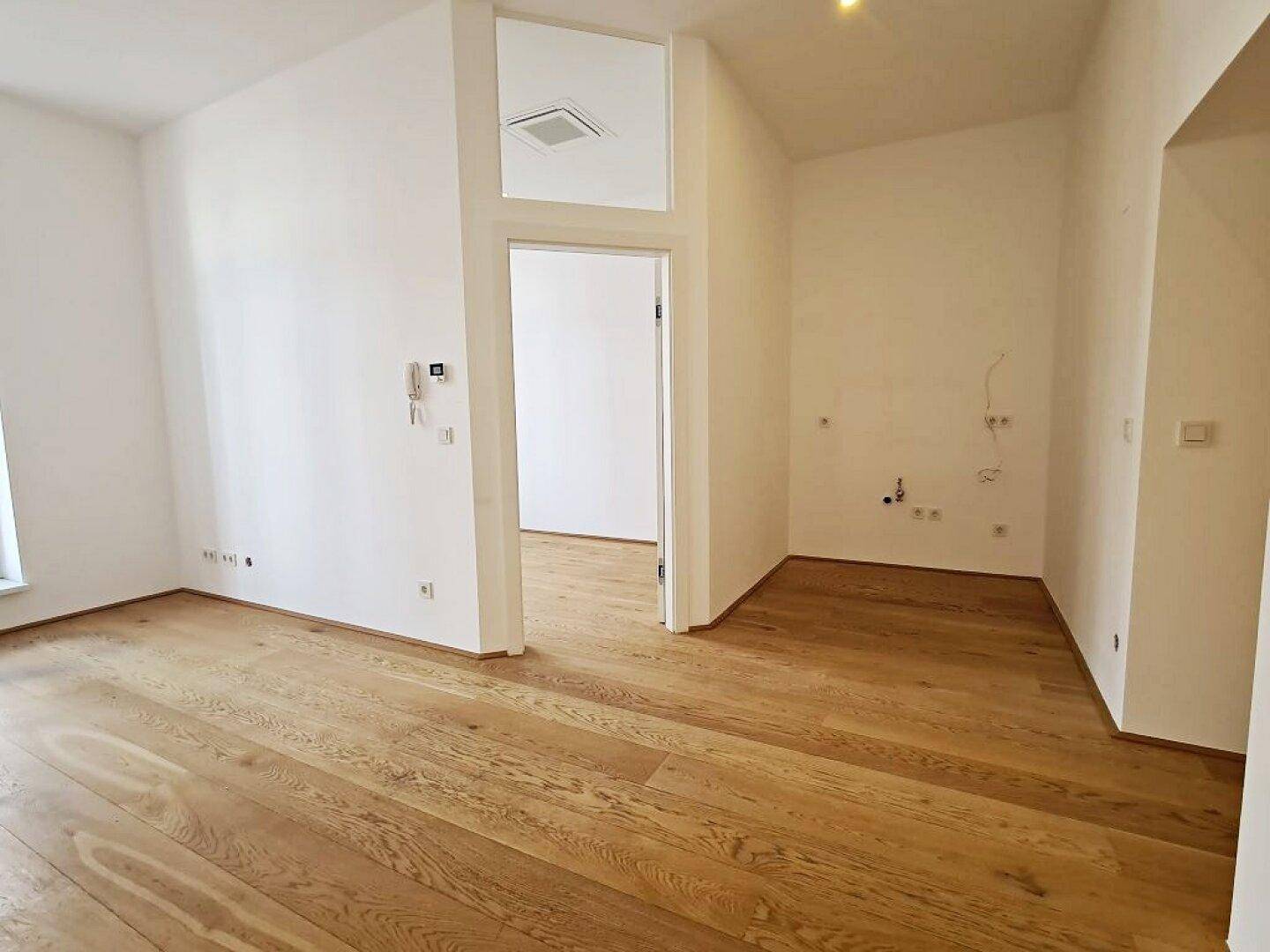Heller Raum mit Holzboden, weißen Wänden und einer offenen Tür, vorbereitet für Elektroinstallationen.