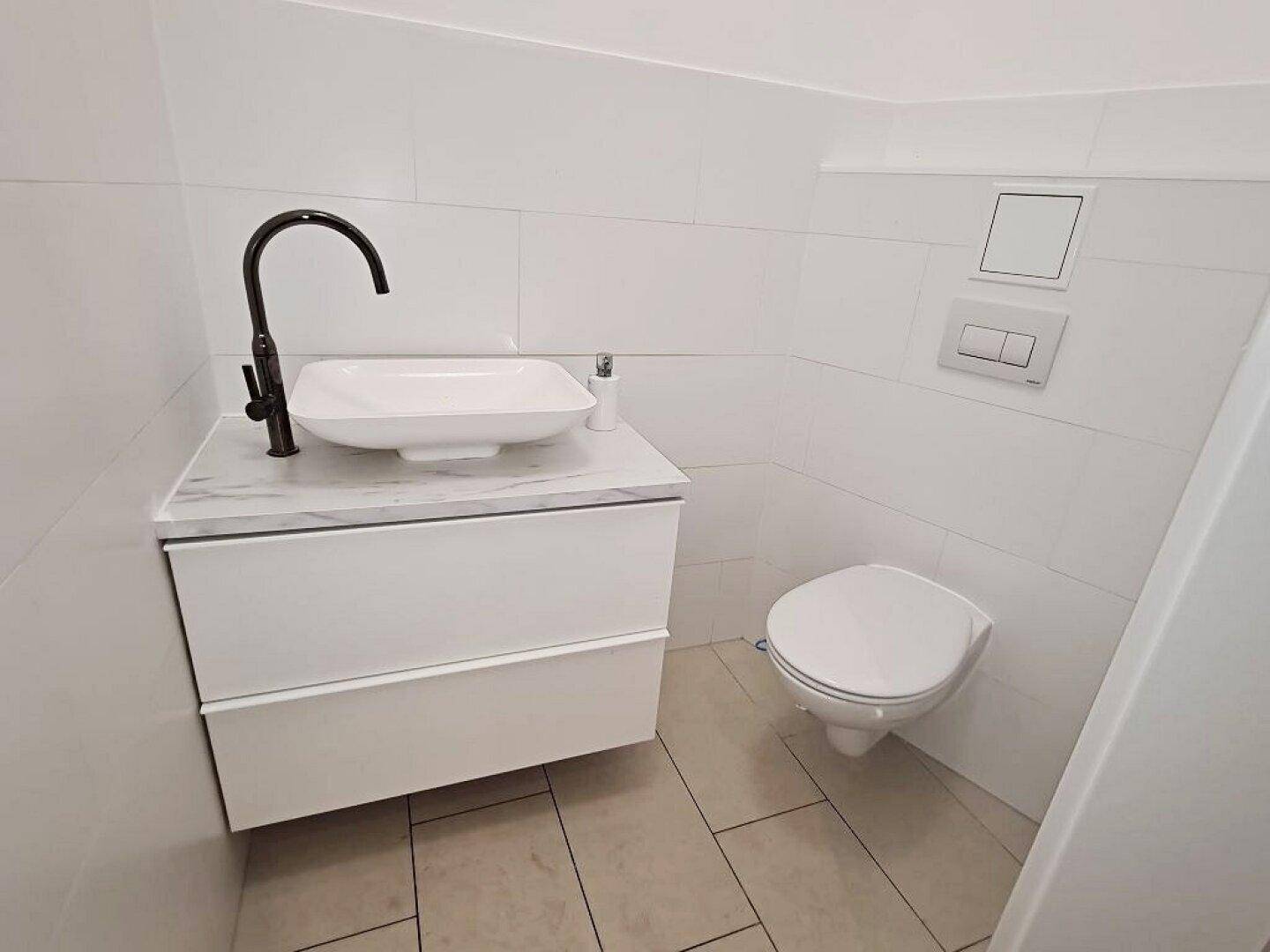 Modernes Badezimmer mit weißen Fliesen, wandhängendem WC und einem stilvollen Waschtisch mit schwarzer Armatur.
