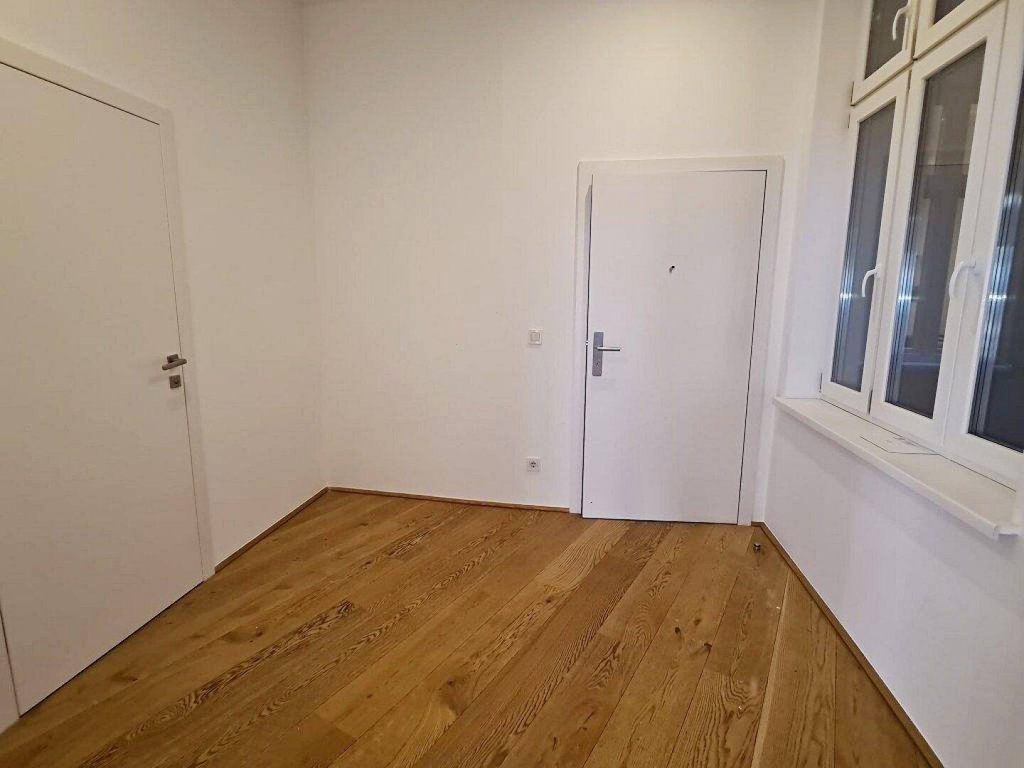 Heller Flur mit Holzdielenboden, weißen Türen und einem Fenster, das natürliches Licht hereinlässt.