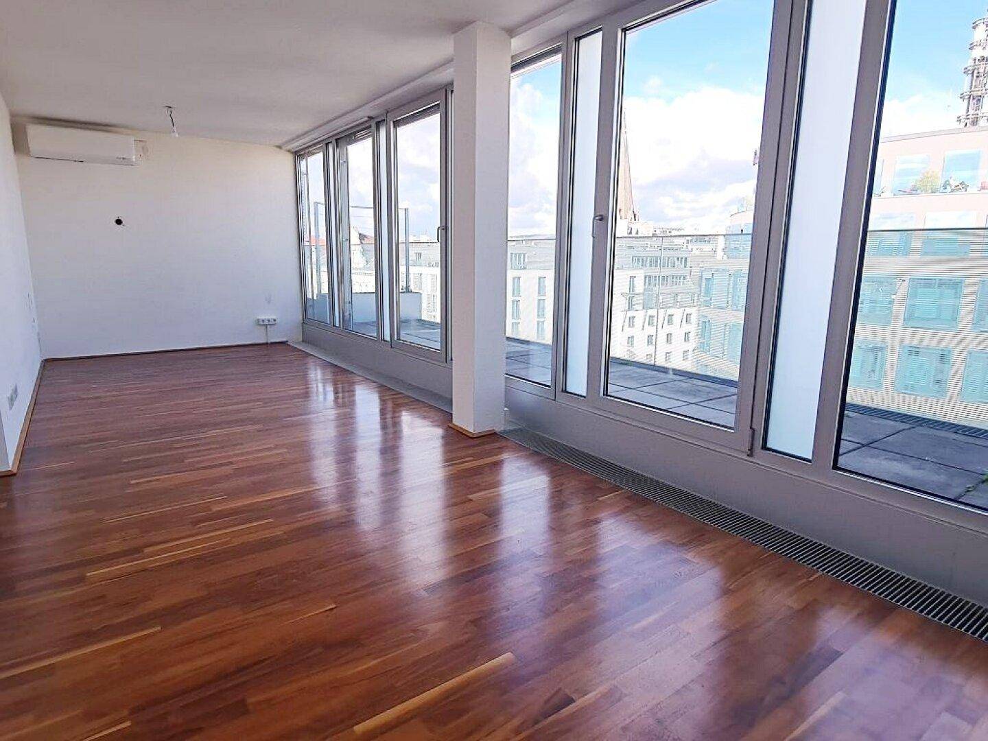 Heller Wohnraum mit Holzboden und großen Fenstern, die viel Tageslicht hereinlassen und Stadtblick bieten.