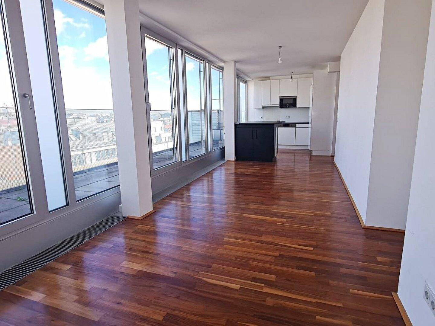 Offener Wohn- und Essbereich mit moderner Küche, Holzboden und großen Fenstern mit Stadtblick.