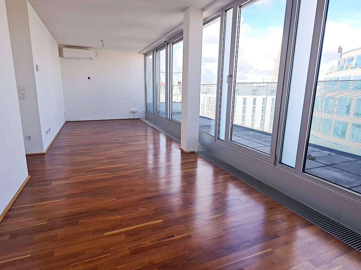 Geräumiger Wohnbereich mit glänzendem Holzboden und raumhohen Fenstern mit Stadtblick.