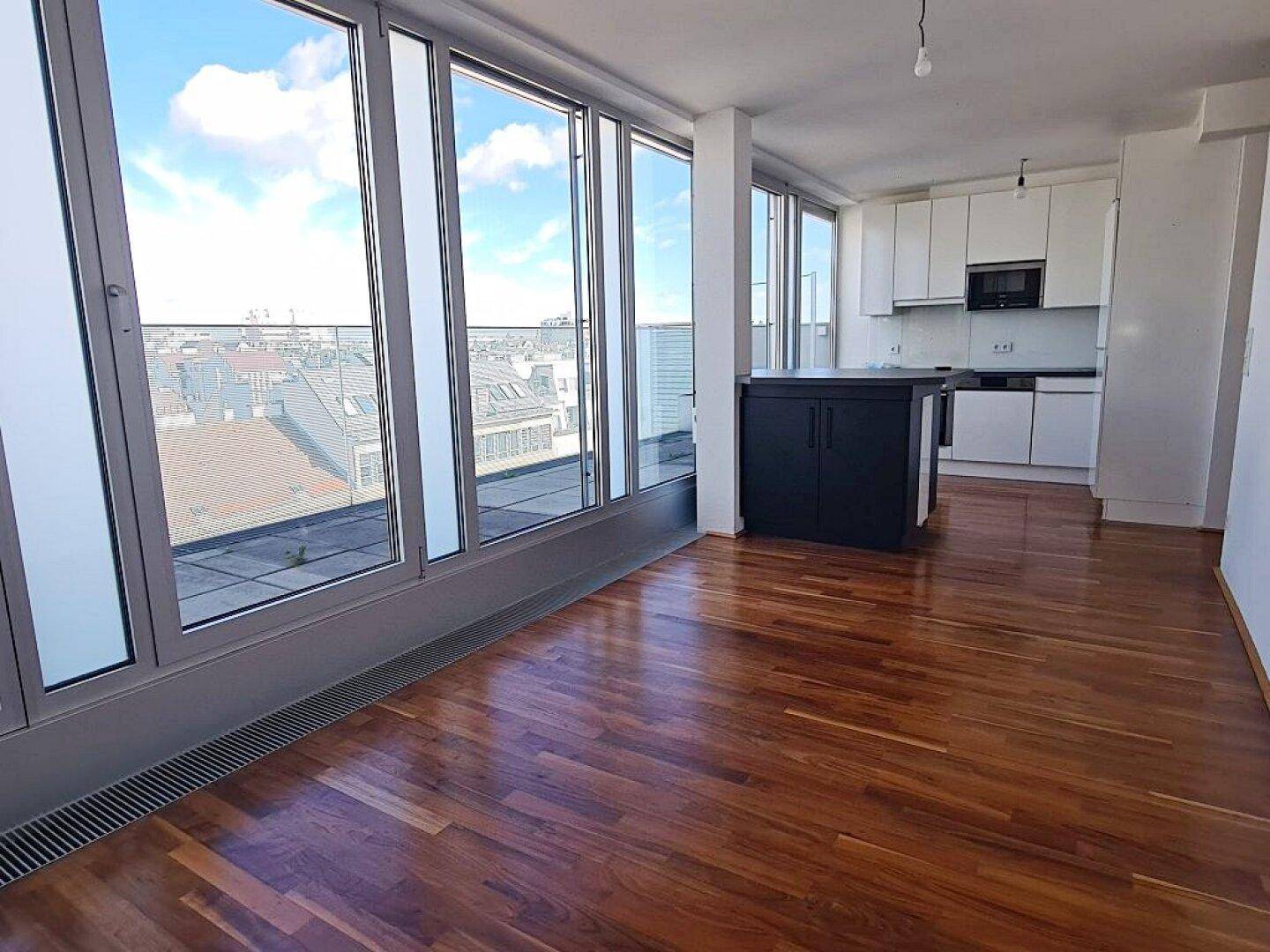 Lichtdurchfluteter Wohnbereich mit integrierter Küche, Holzboden und weitem Ausblick auf die Stadt.