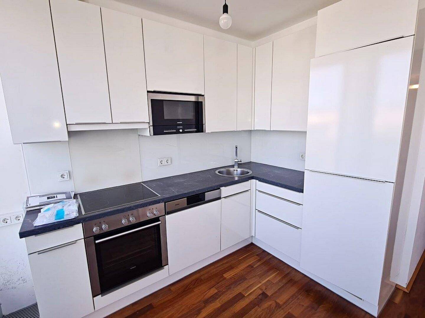 Helle, moderne Einbauküche mit weißen Fronten, integrierten Geräten und dunkler Arbeitsplatte.