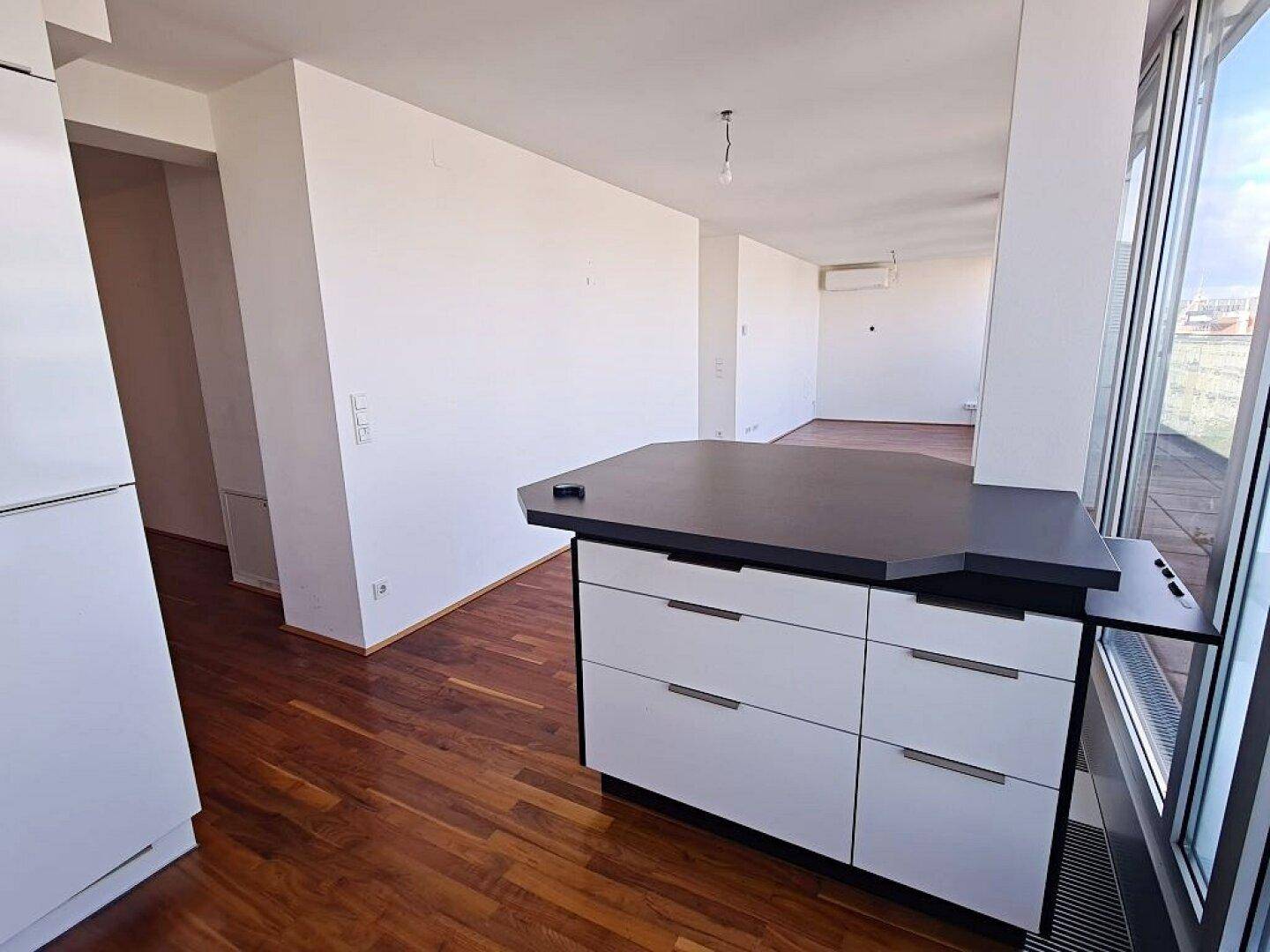 Offener Wohnbereich mit Holzboden, Kücheninsel und Zugang zu weiteren Räumen der Wohnung.
