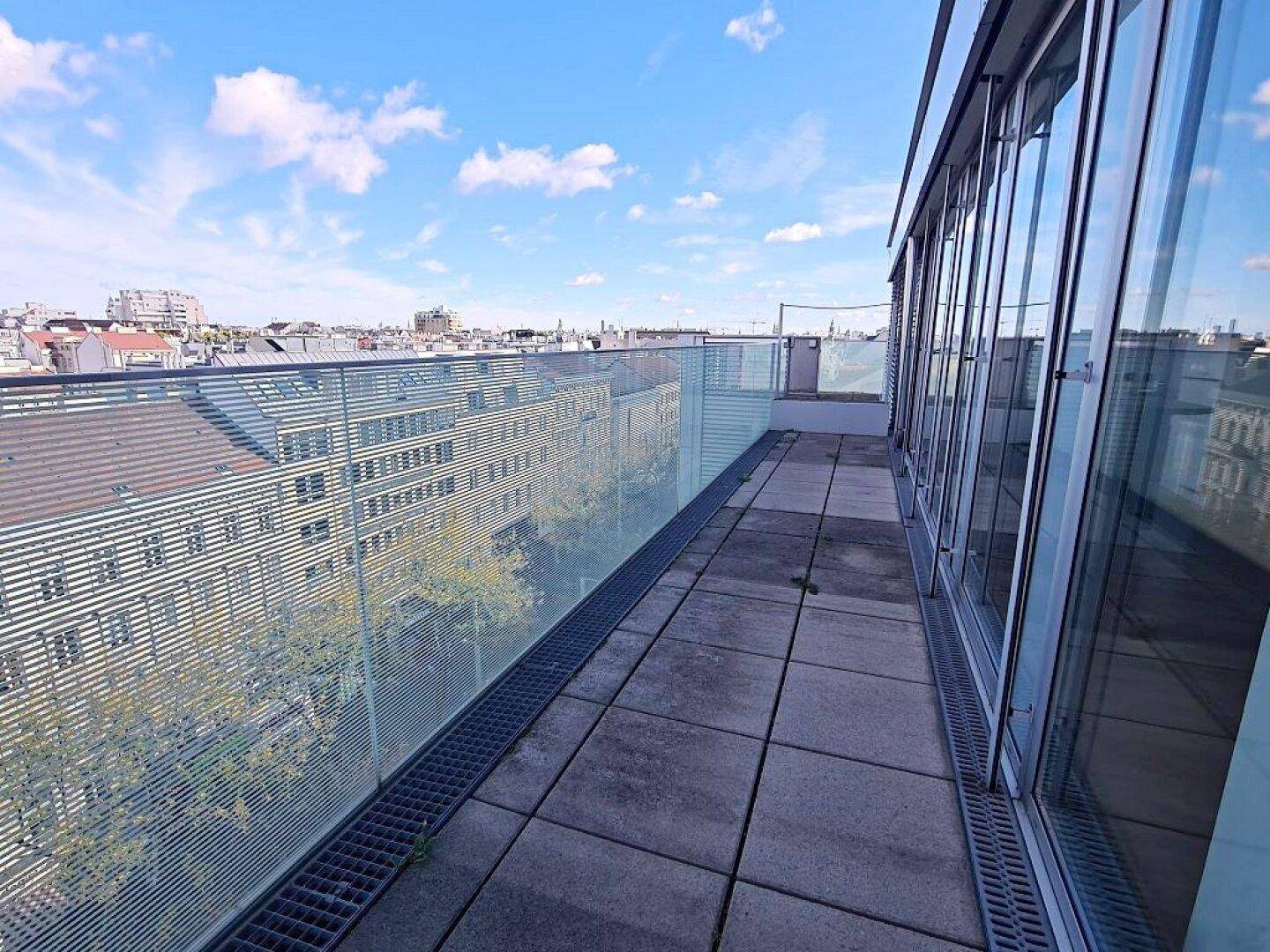 Lange Terrasse mit Glasgeländer und Blick auf die umliegenden Gebäude und die Stadtlandschaft.