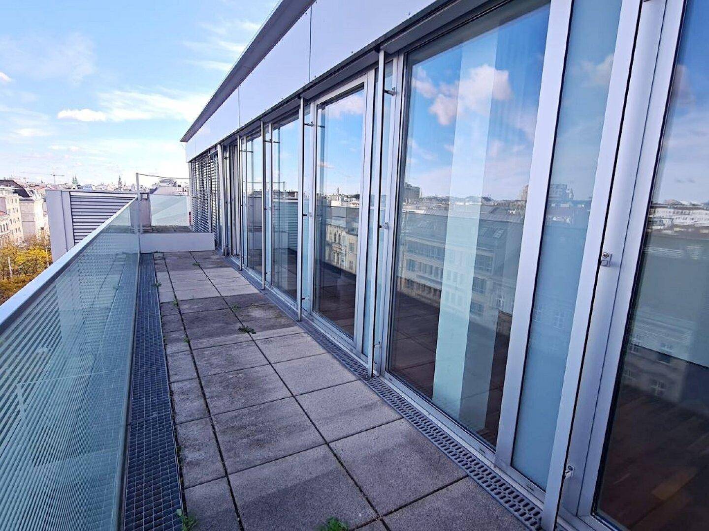 Lange Terrasse mit Glasgeländer und Zugang zu den Innenräumen durch große Fensterfronten.