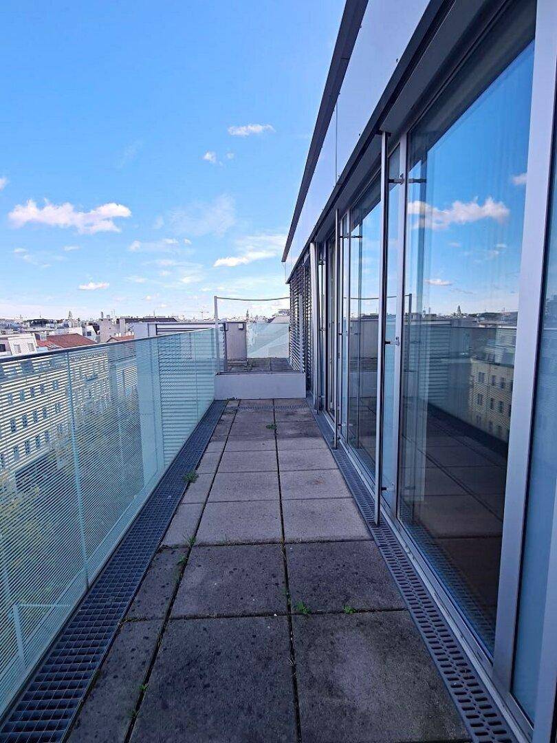 Sonniger Terrassenbereich mit Glasgeländer und weitem Blick über die Stadtlandschaft und den Himmel.