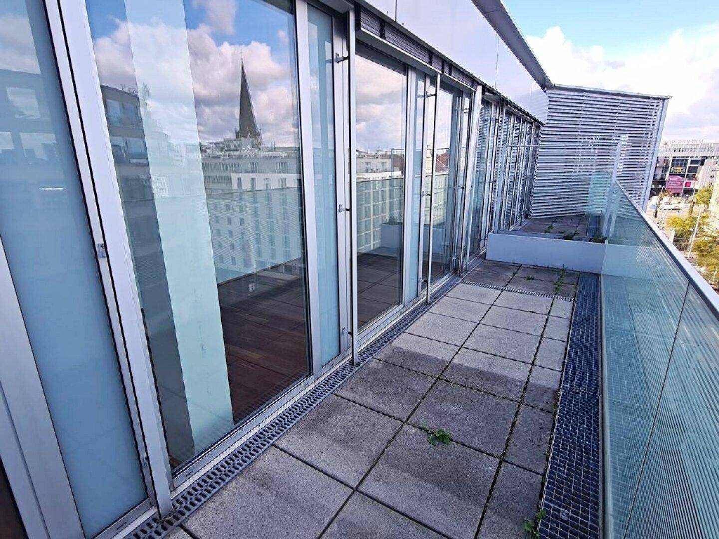 Terrasse mit großen Fenstern und Glasgeländer, bietet einen weiten Blick über die Stadt.