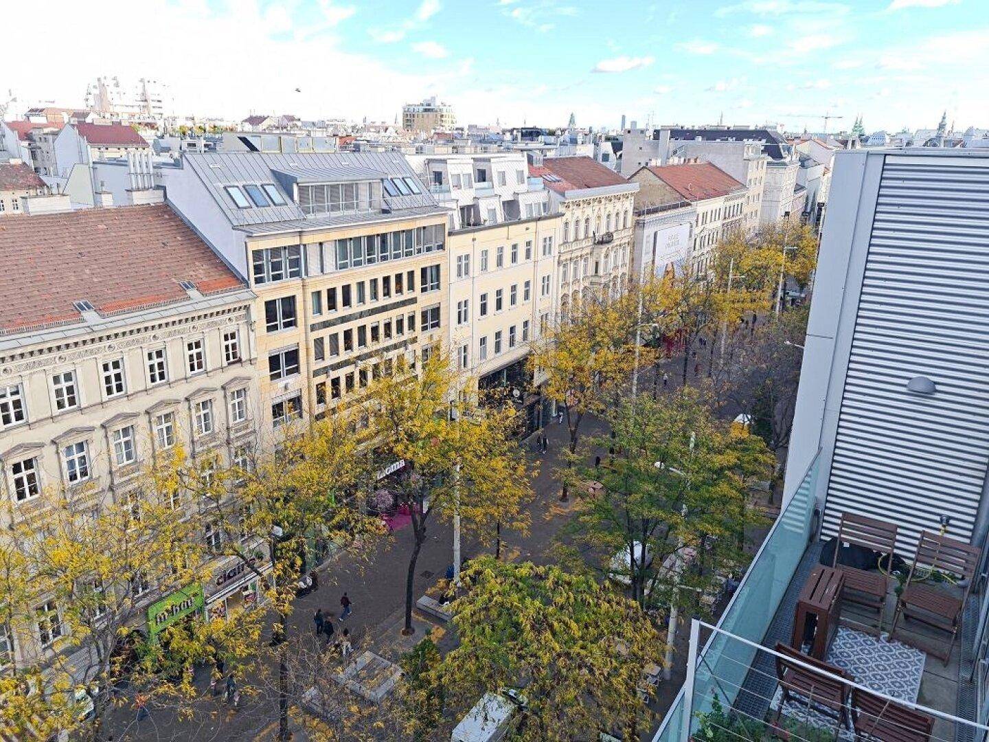 Dachterrasse mit Sitzgelegenheiten und Panoramablick auf die belebte Stadtstraße mit Bäumen.