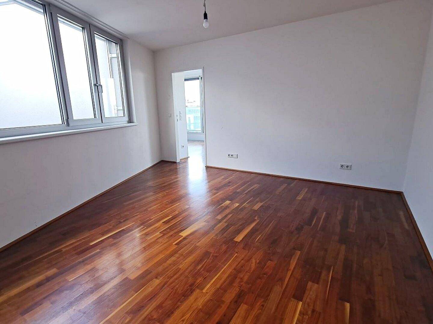 Heller, leerer Raum mit Holzboden und Fenstern, ideal als Wohn- oder Schlafzimmer nutzbar.