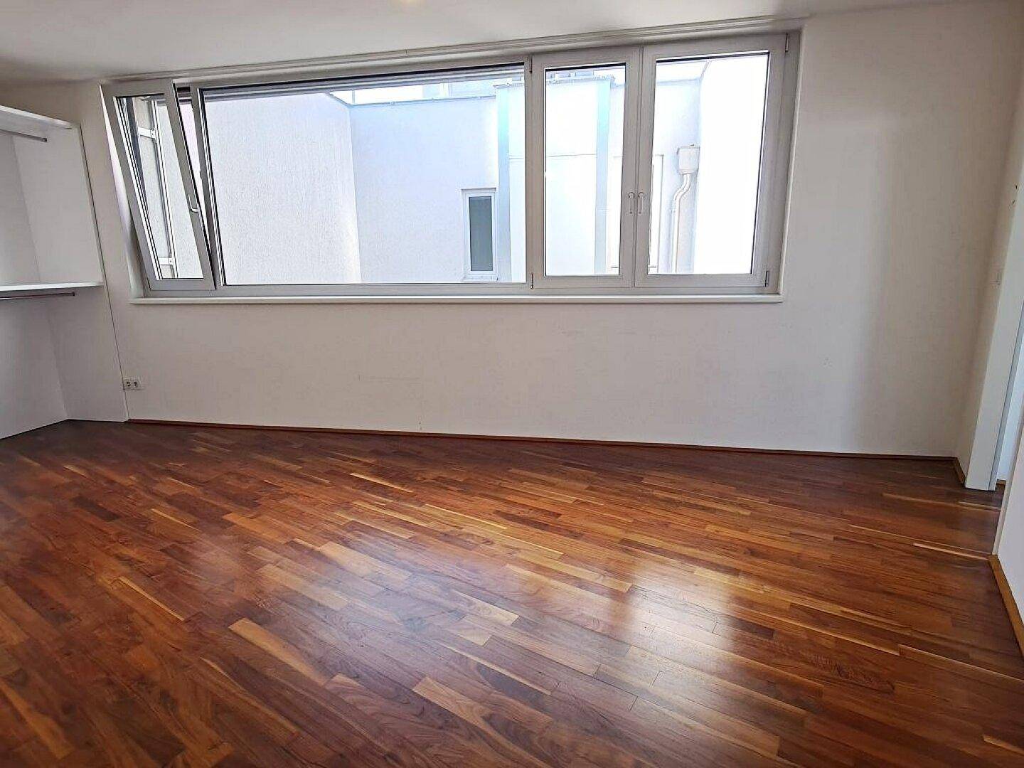 Heller Raum mit großen Fenstern und dunklem Holzparkett, ideal als Schlafzimmer.