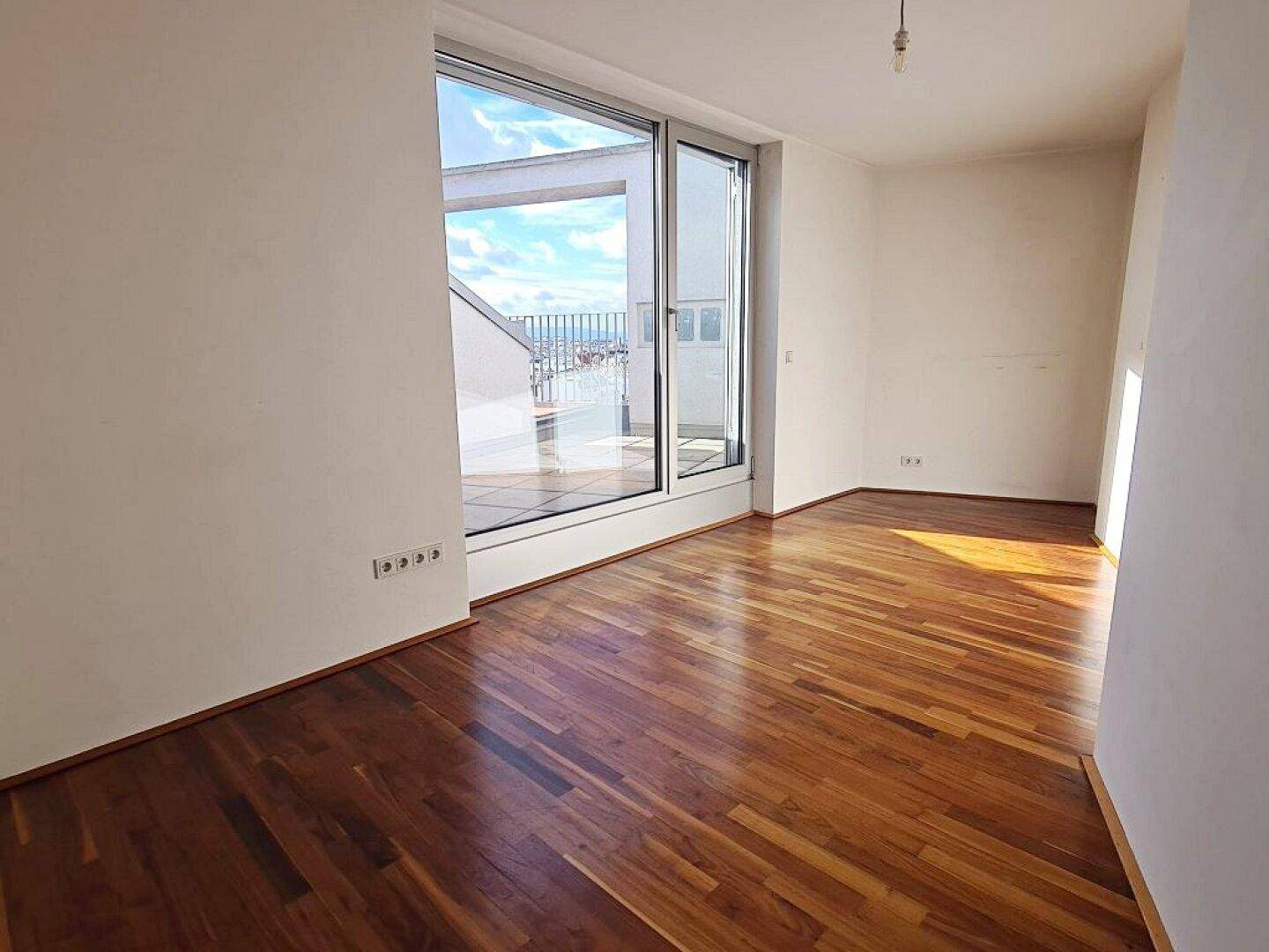 Lichtdurchfluteter Wohnraum mit Zugang zur Terrasse und dunklem Parkettboden.