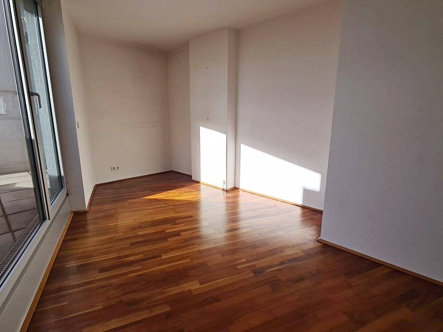 Heller Wohnbereich mit Holzboden und viel Tageslicht durch große Fenster.