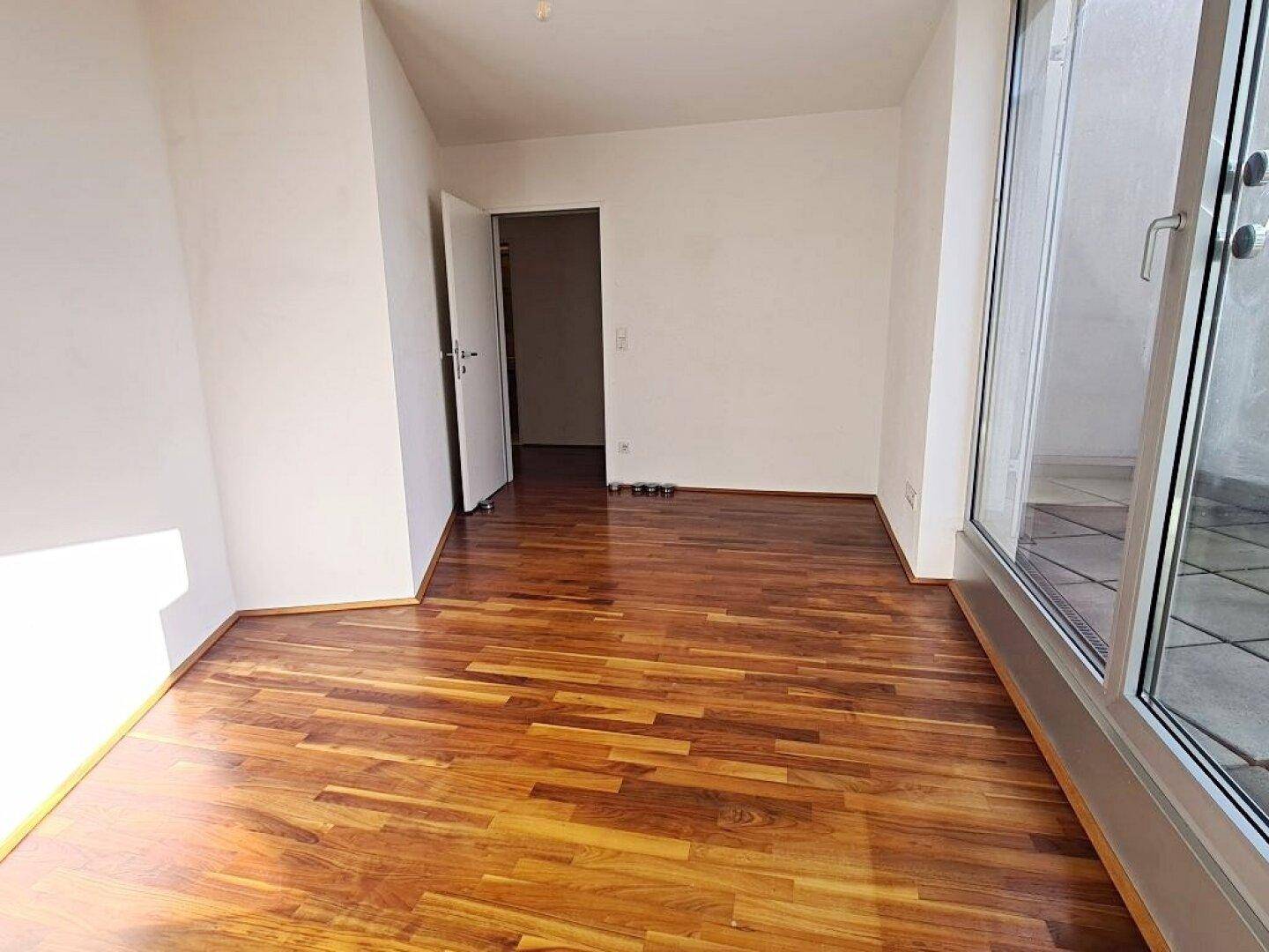 Geräumiger Wohnraum mit Parkettboden und Zugang zu einem weiteren Zimmer.