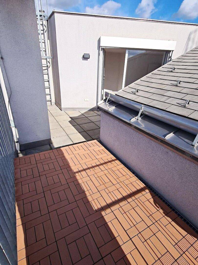 Balkon mit Holzdielen und Blick auf die Dächer der Stadt und eine weitere Terrasse.