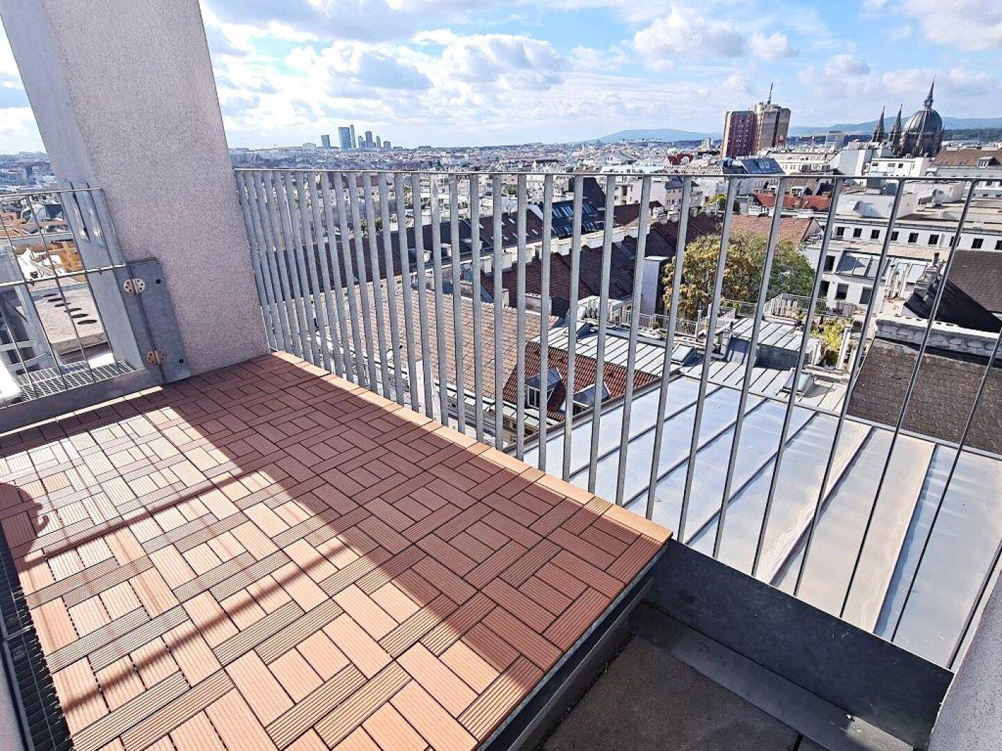 Sonniger Balkon mit Holzboden und beeindruckendem Blick auf die Stadtlandschaft.