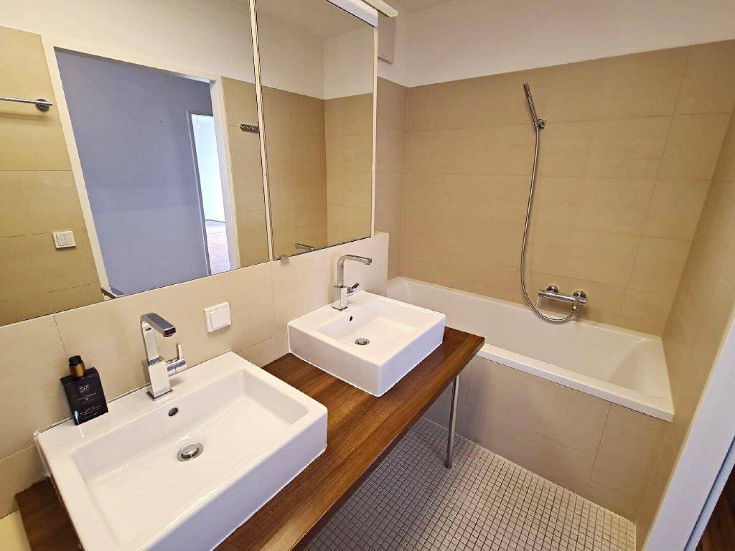 Helles Badezimmer mit Doppelwaschbecken, Badewanne und beigefarbenen Wandfliesen.
