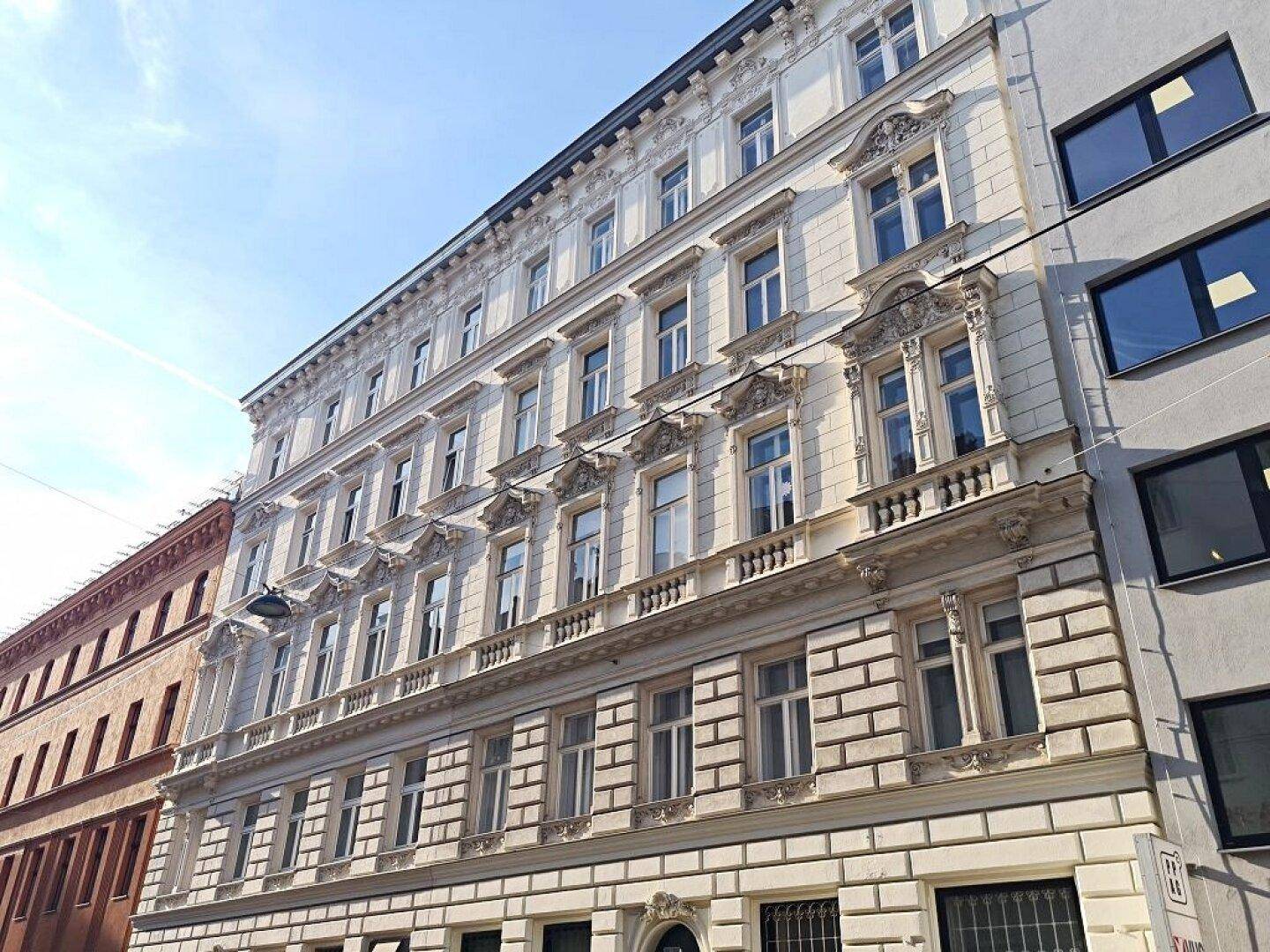 Prächtige Altbaufassade mit detaillierten Verzierungen und vielen Fenstern unter klarem Himmel.