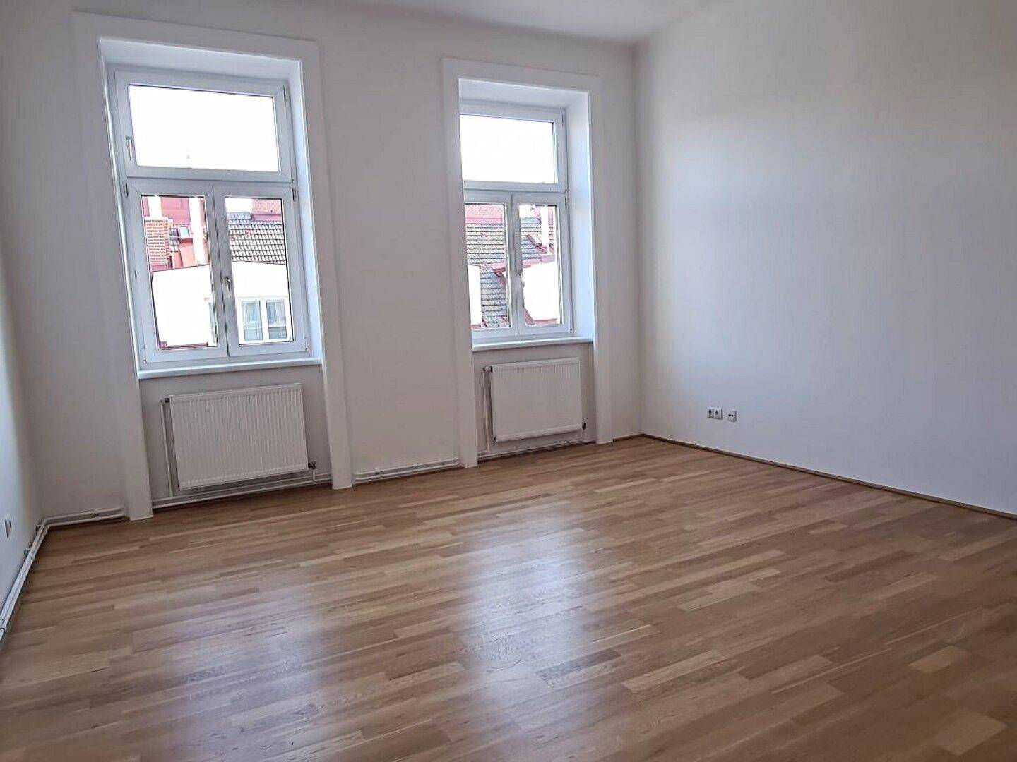 Geräumiges Zimmer mit hellem Parkettboden und zwei großen Fenstern, bereit zur individuellen Gestaltung.