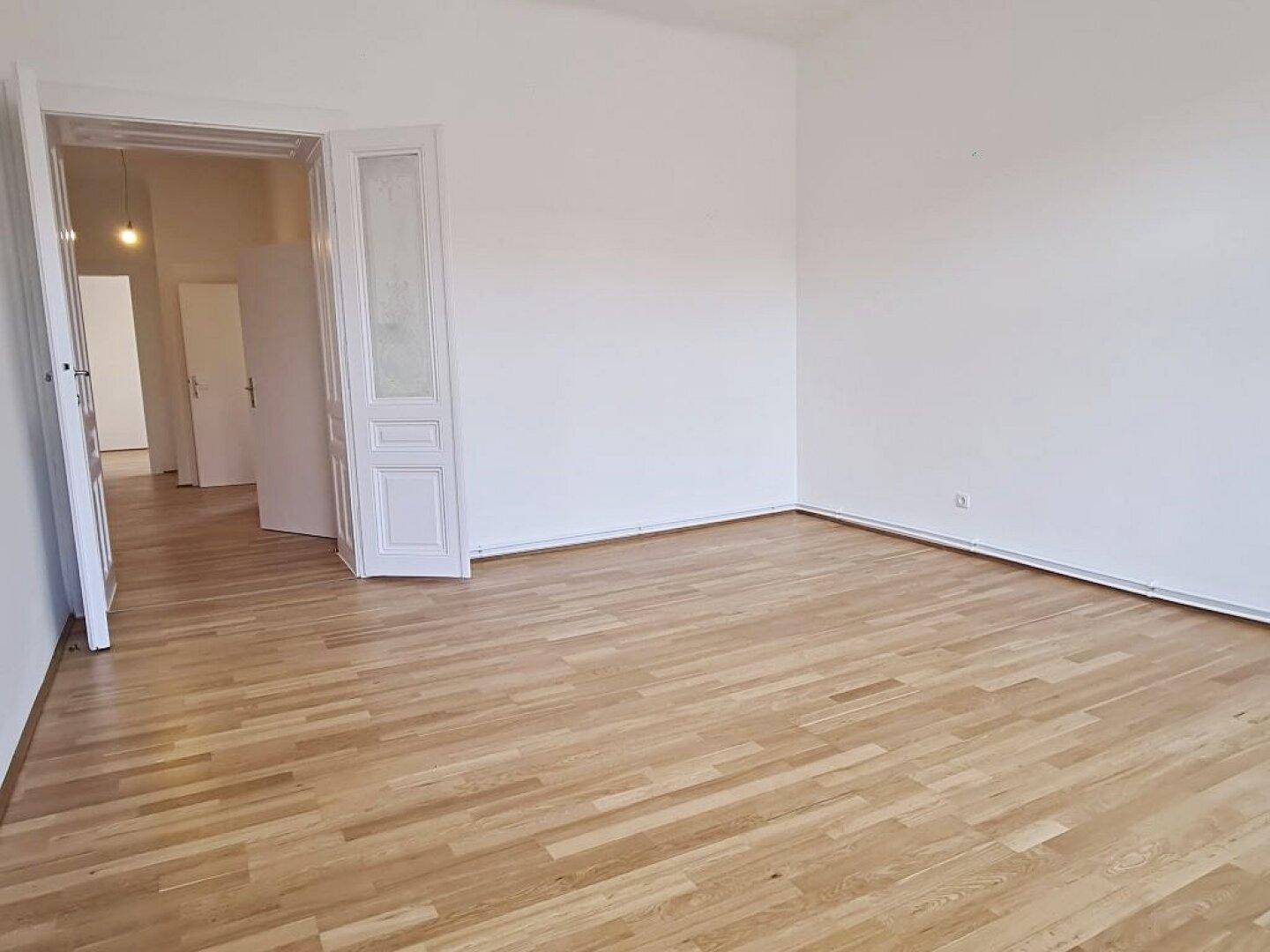 Lichtdurchflutetes Zimmer mit Parkettboden und offenem Zugang zu einem Flur, ideal für flexible Nutzung.