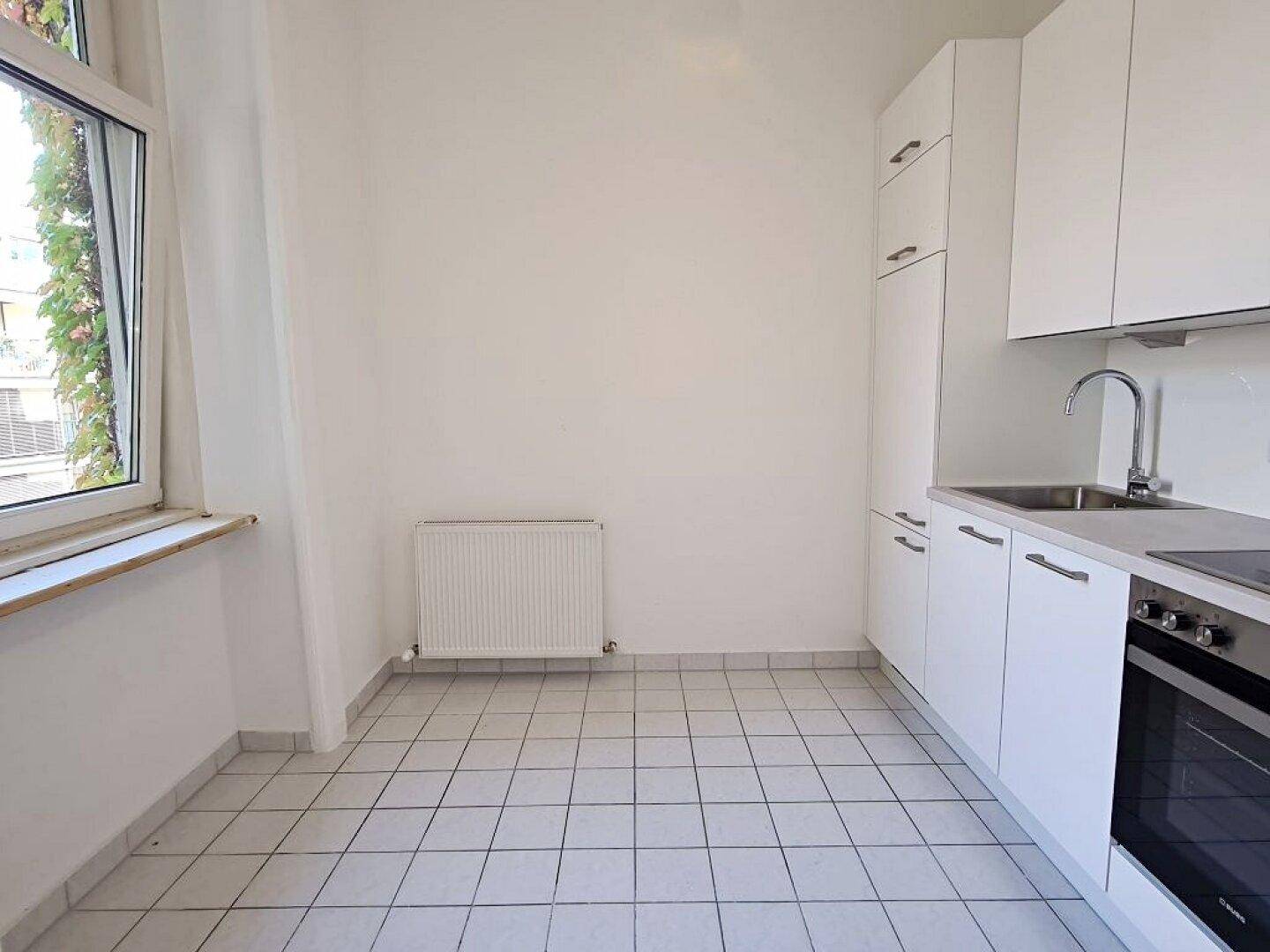 Helle Küche mit weißen Schränken, Spüle und Fenster, bietet Platz für einen Essbereich.