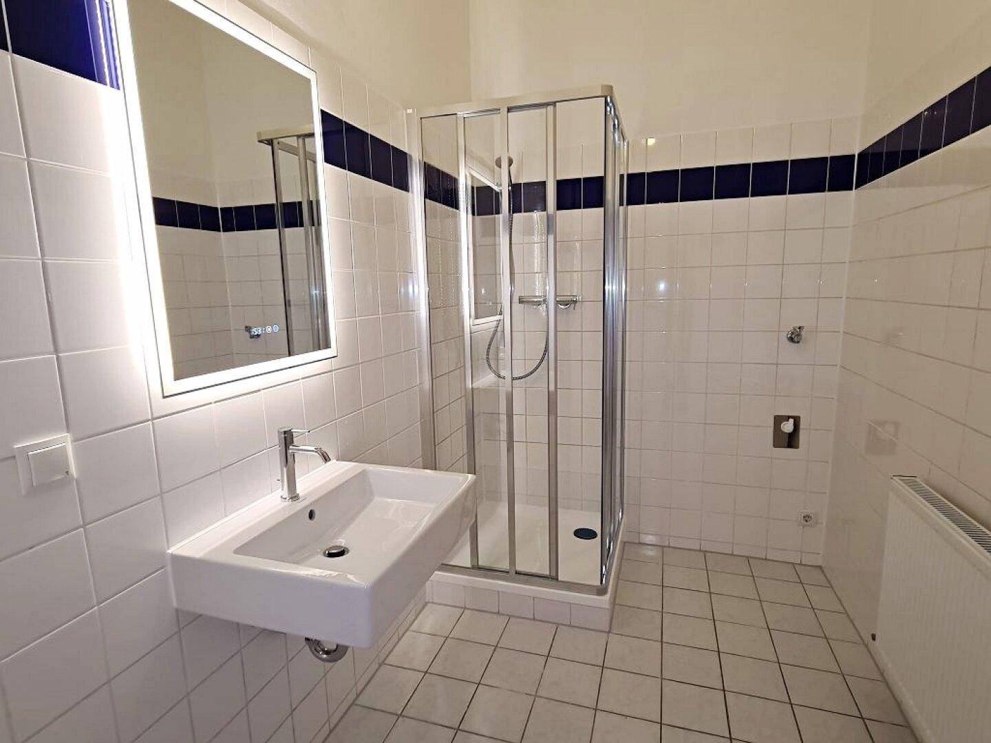 Modernes Badezimmer mit weißen Fliesen, blauer Akzentleiste, Waschbecken und Duschkabine.