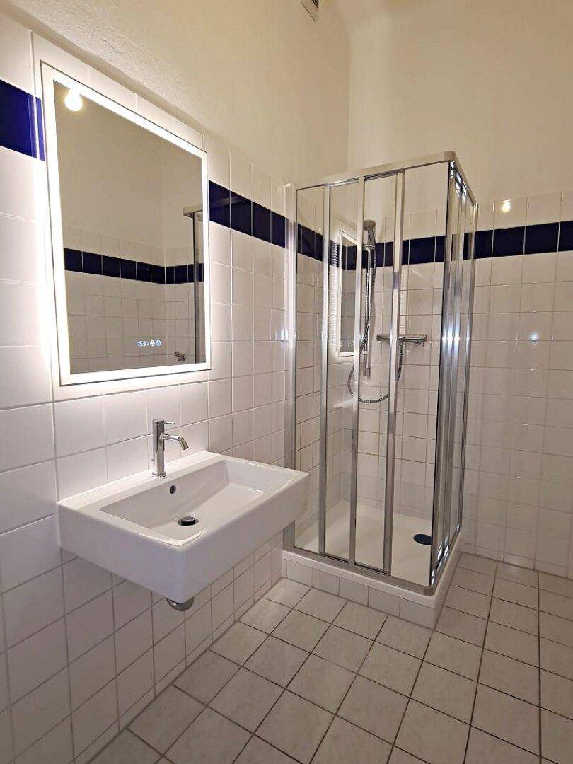 Helles Badezimmer mit Duschkabine, modernem Waschbecken und beleuchtetem Spiegel.