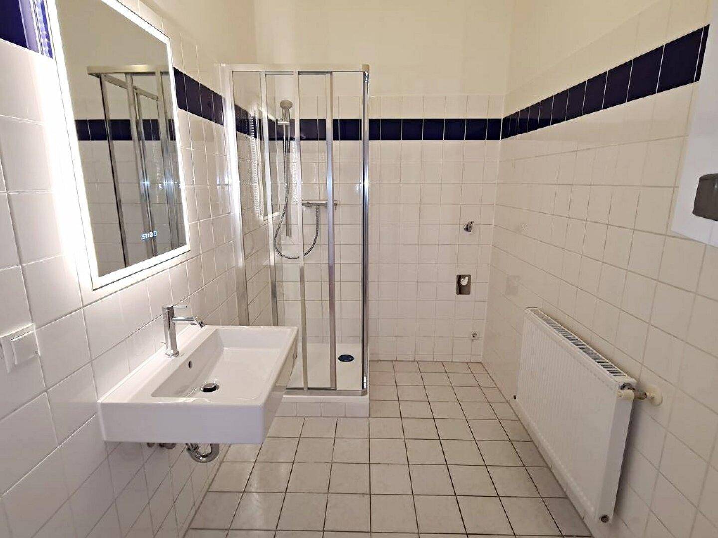Funktionales Badezimmer mit weißen Fliesen, Duschkabine und Heizkörper, sauber und gepflegt.