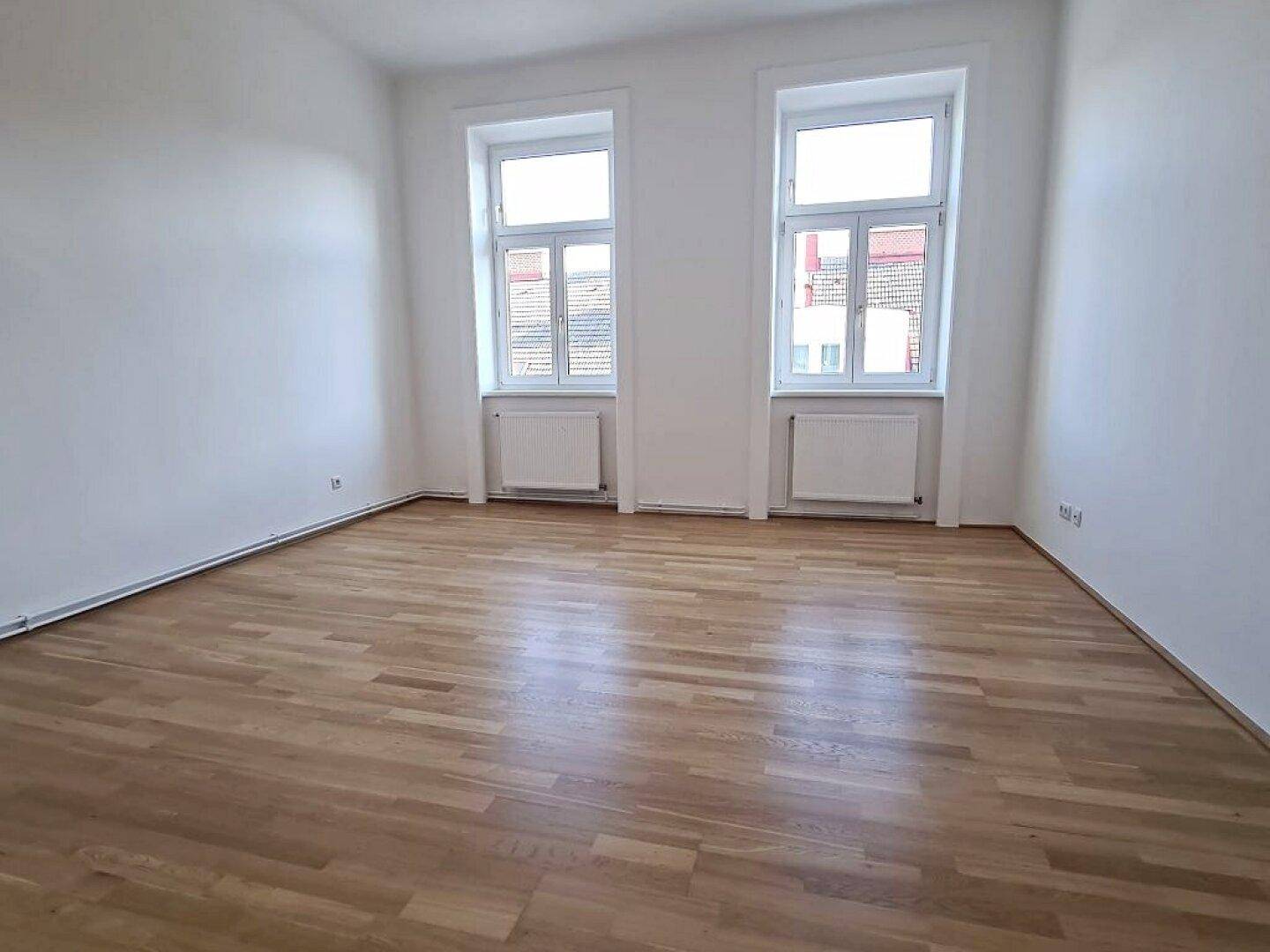Geräumiges Zimmer mit hellem Parkettboden und zwei großen Fenstern, bereit zur individuellen Gestaltung.