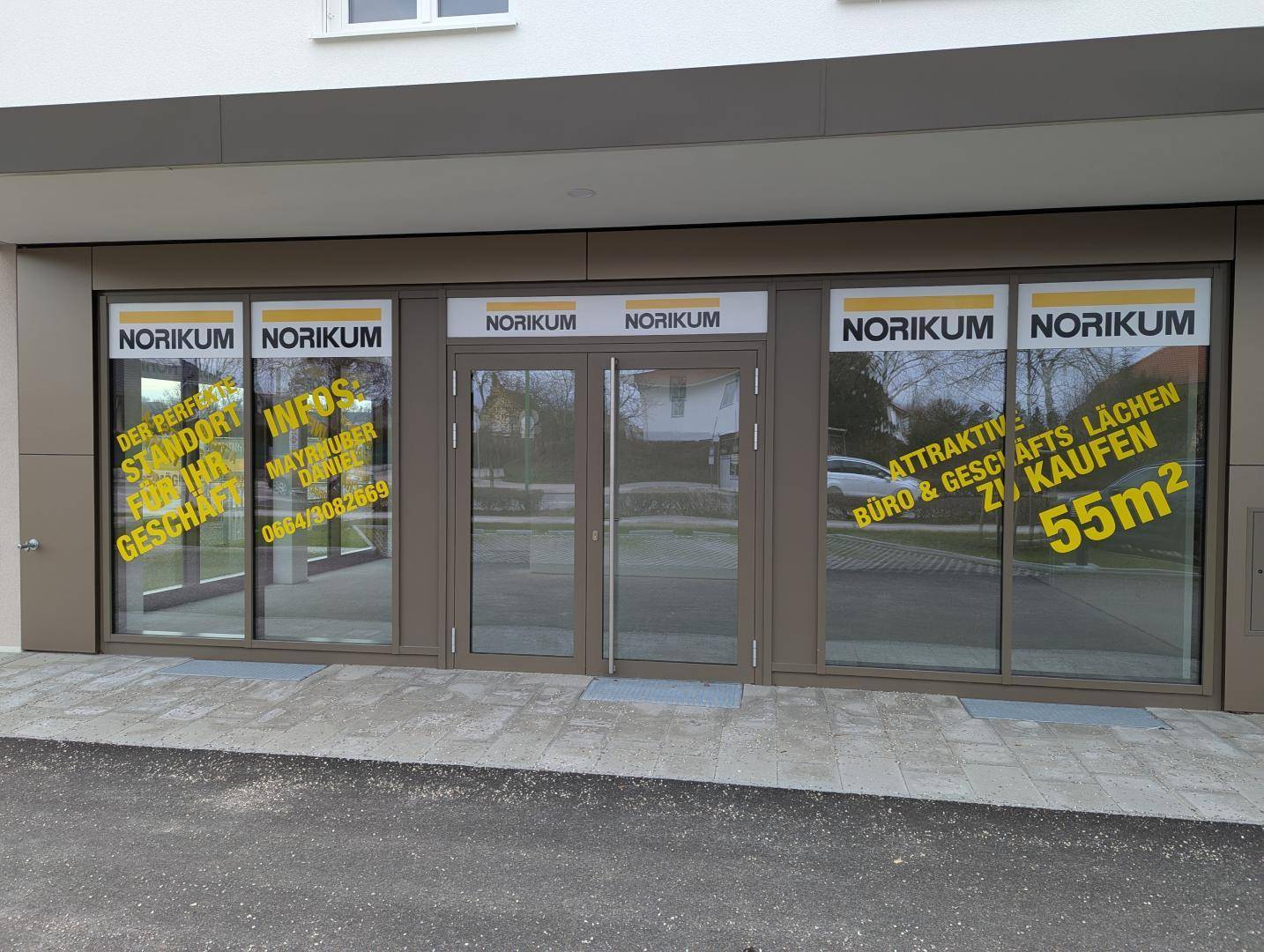Eingangsbereich eines modernen Geschäftsgebäudes mit großen Fenstern und Doppeltüren.