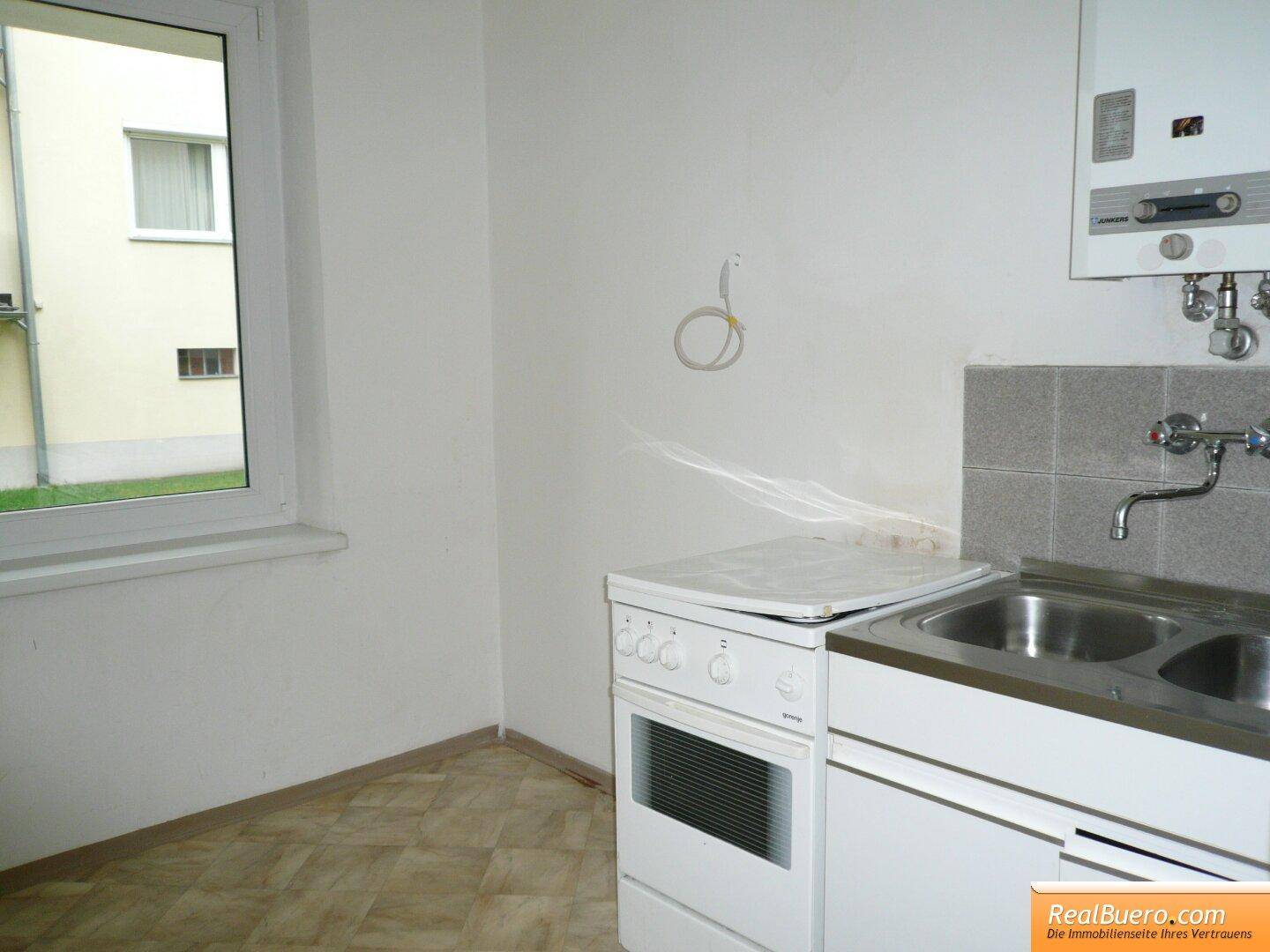 Küchenbereich mit Fenster für natürliche Belichtung, ausgestattet mit Spüle und kleinem Elektroherd.