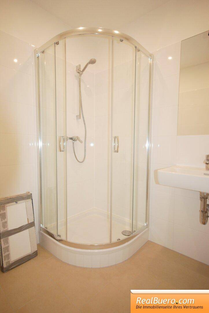 Modernes Badezimmer mit Duschkabine, weißem Waschbecken und hellen Fliesen.