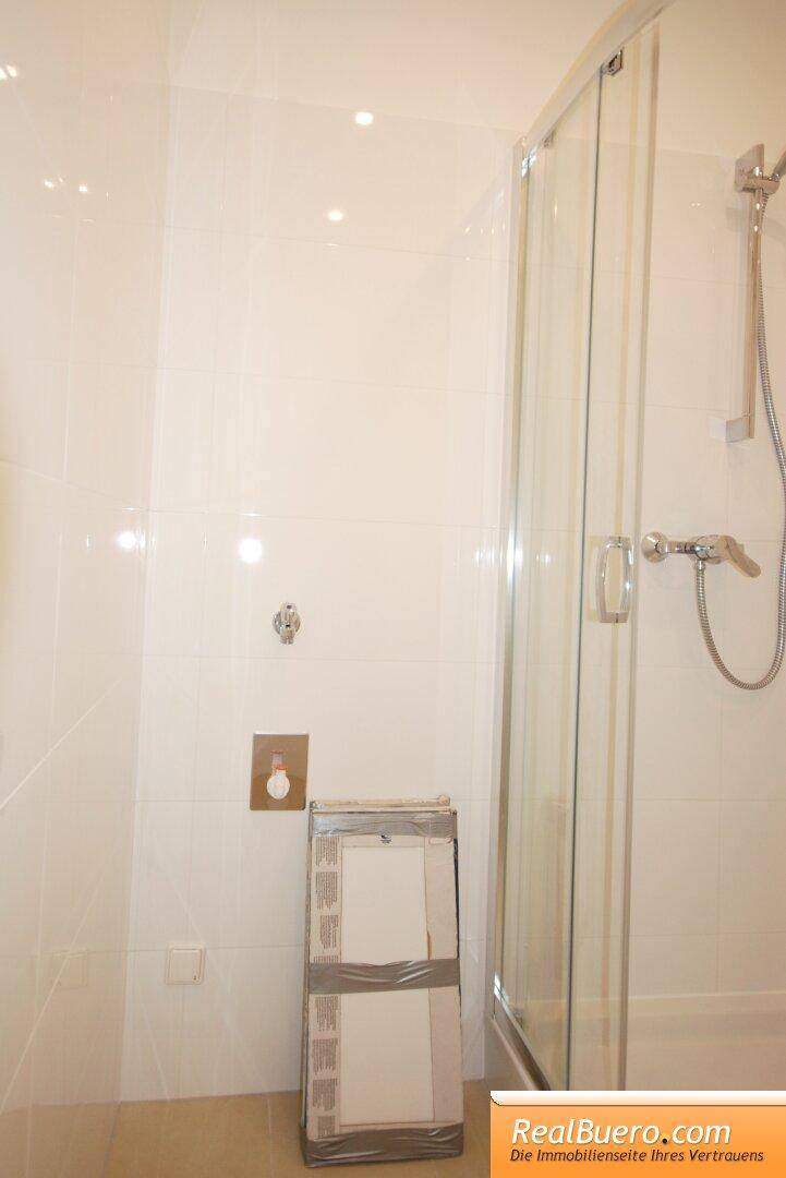 Detaillierte Ansicht der Duschkabine mit Glaswänden und weißen Fliesen im Badezimmer.