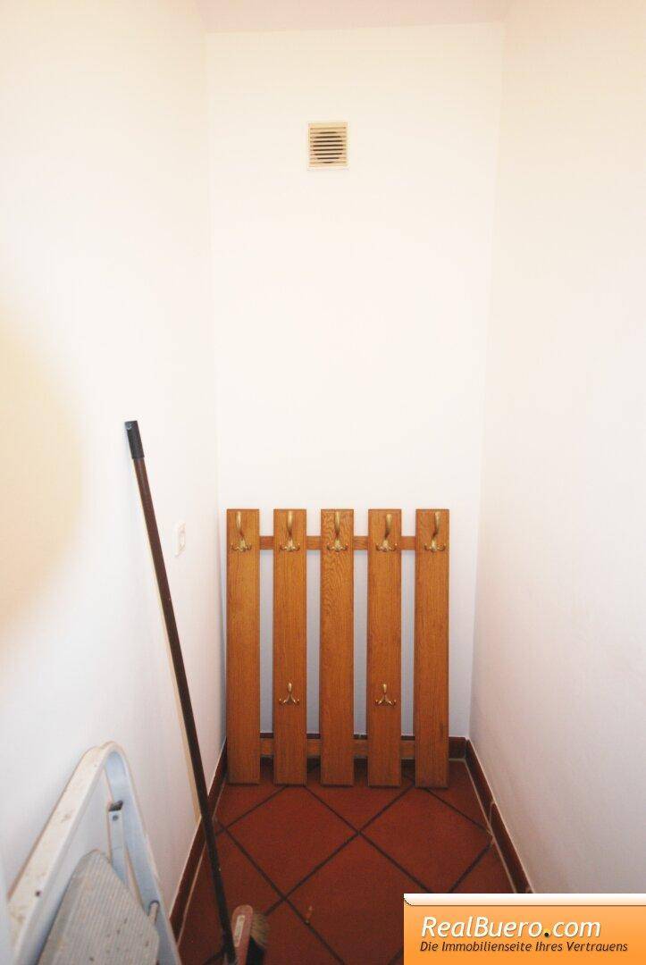 Schmaler Flur mit Fliesenboden und einer hölzernen Garderobe an der Wand.