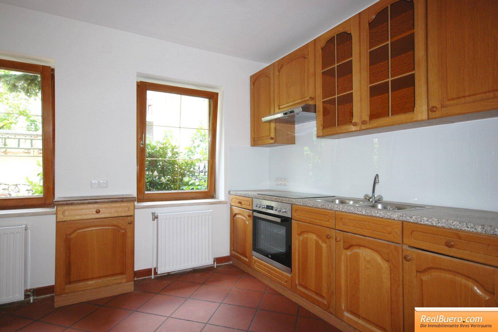 Funktionale Küche mit Holzschränken, integrierten Geräten und Terrakotta-Fliesenboden.