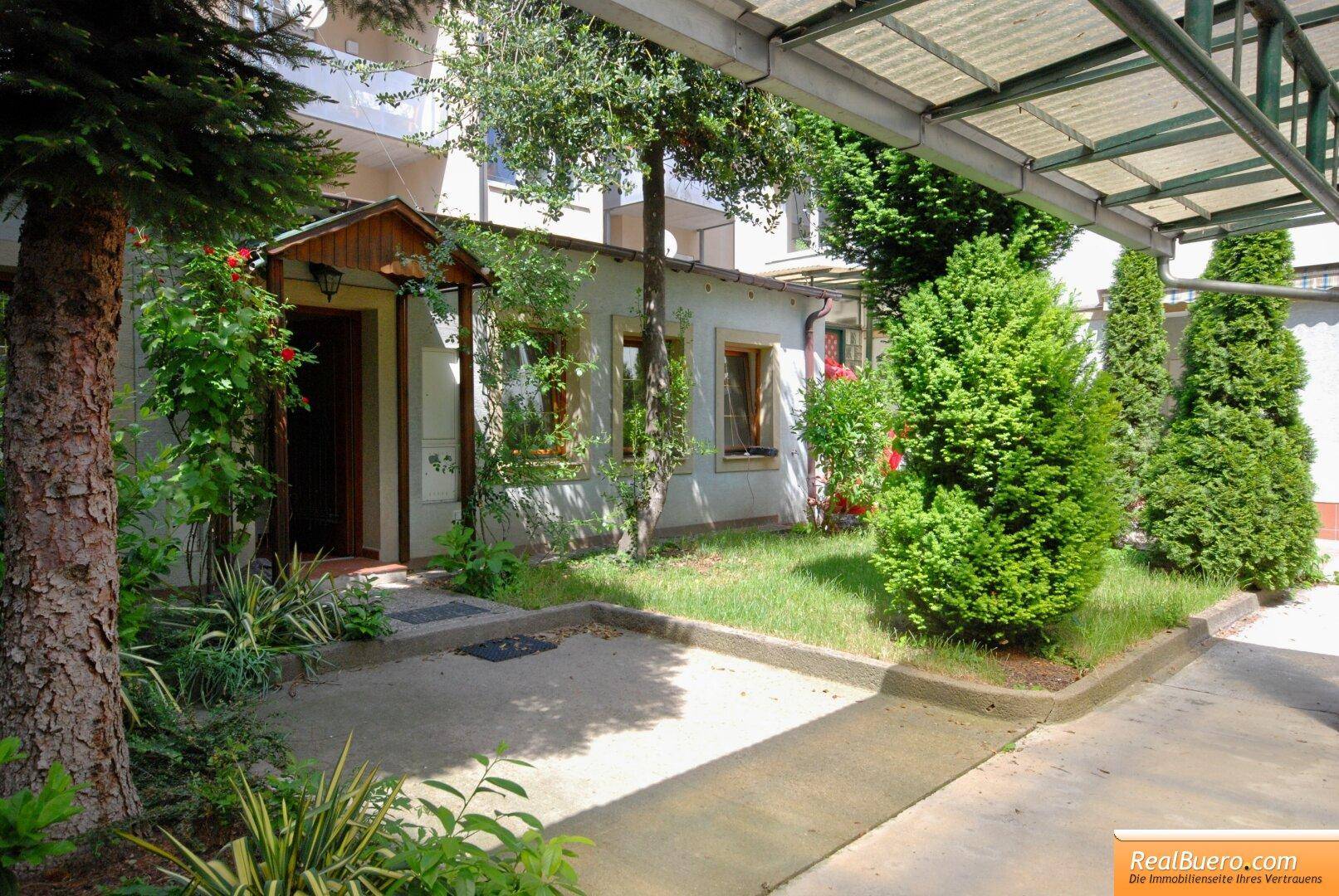 Eingangsbereich des Hauses mit Garten und einem überdachten Stellplatz für Fahrzeuge.