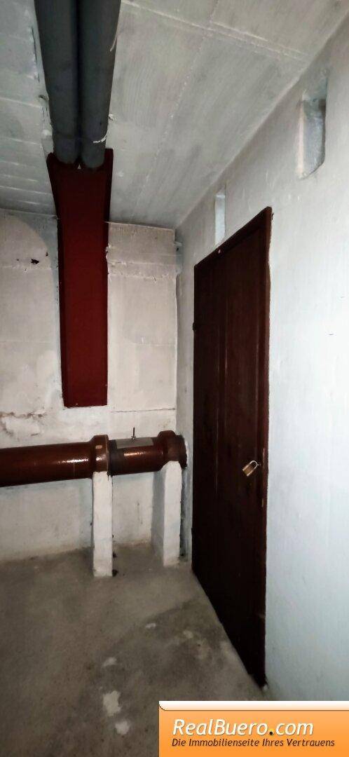 Kellerabteil mit Betonwänden, sichtbaren Rohren und einer robusten Holztür für zusätzlichen Stauraum.