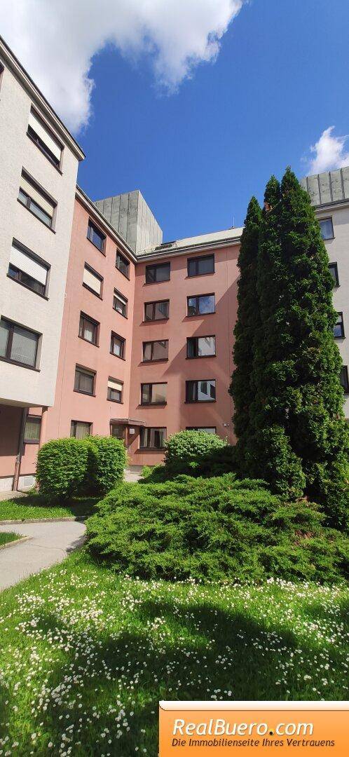 Wohngebäude mit gepflegten Grünflächen, Bäumen und Sträuchern unter blauem Himmel.