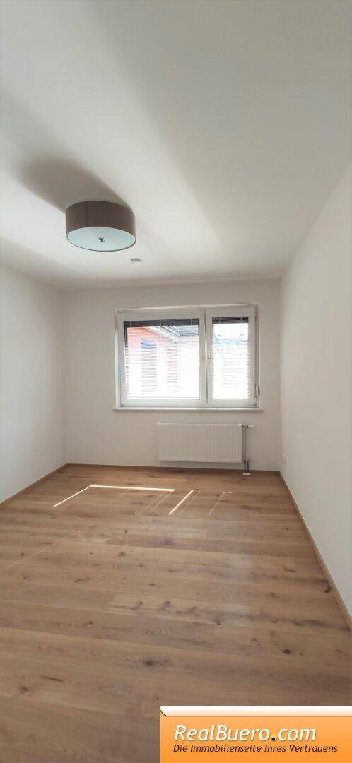 Helles Schlafzimmer mit Parkettboden und großem Fenster für viel Tageslicht, bereit zur individuellen Gestaltung.