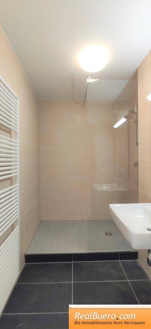 Geräumige ebenerdige Dusche im modernen Badezimmer mit beigen Wandfliesen und Glasabtrennung.