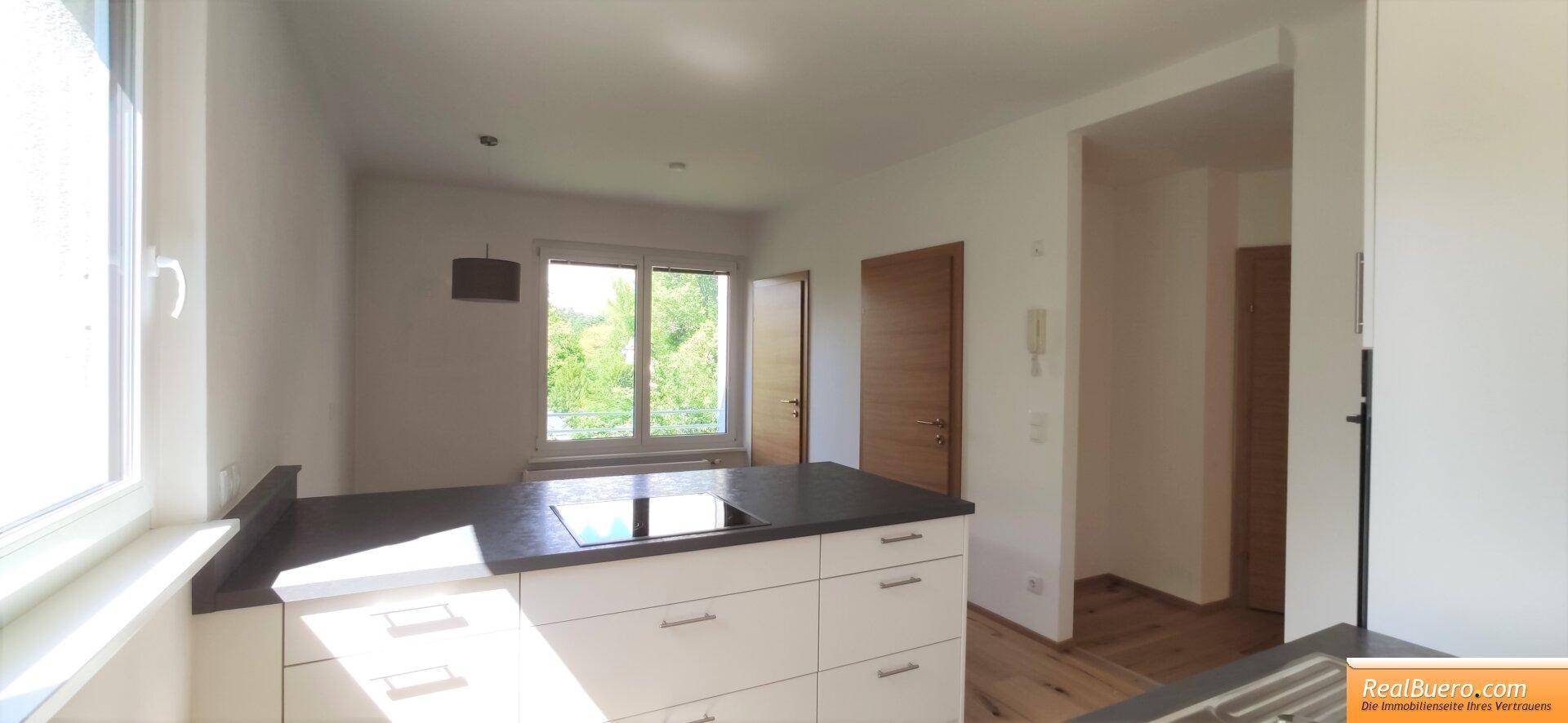 Moderne Küche mit dunkler Arbeitsplatte, Kochfeld und Blick ins Grüne.